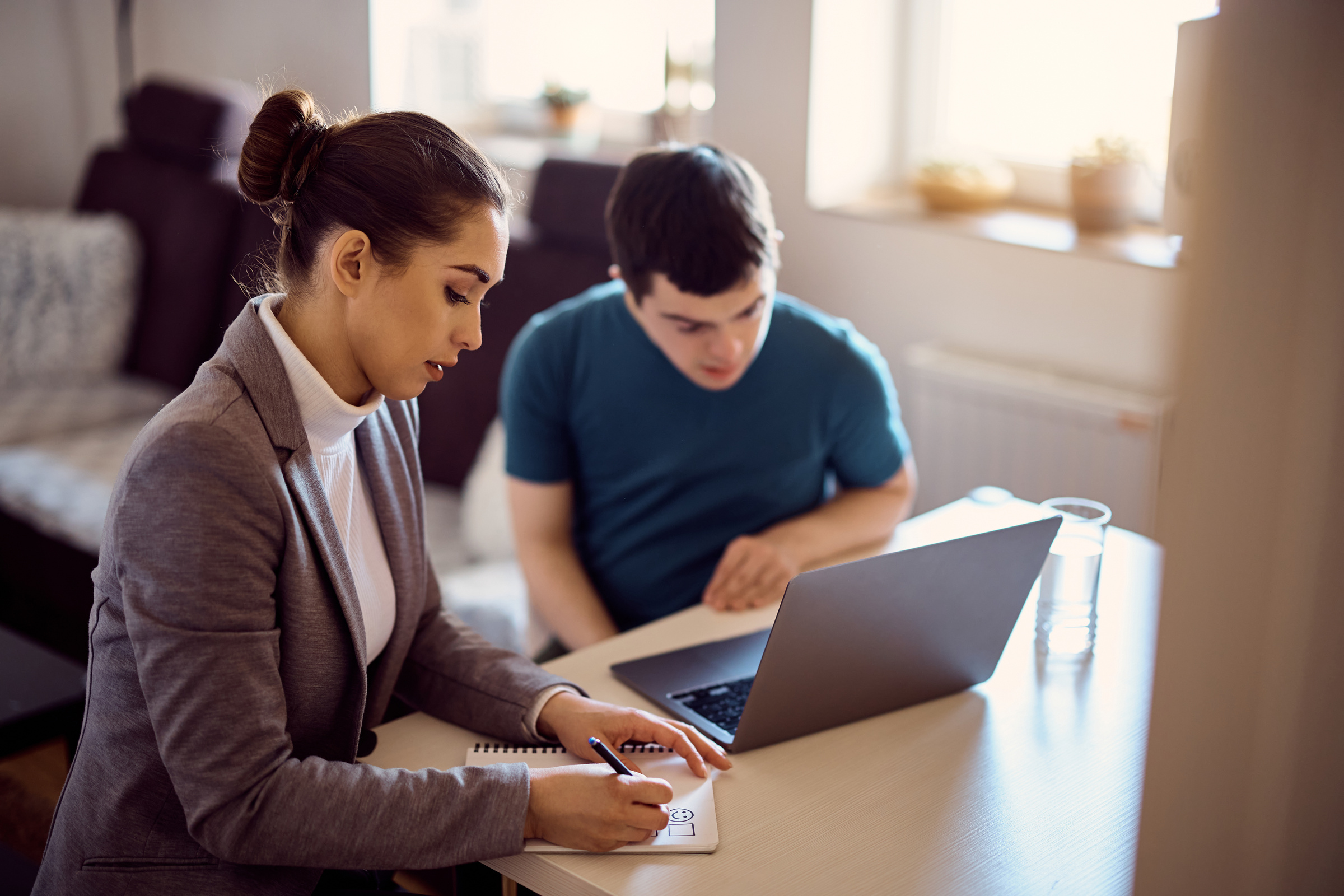 Special education teacher evaluation student with down syndrome who is using laptop at home.